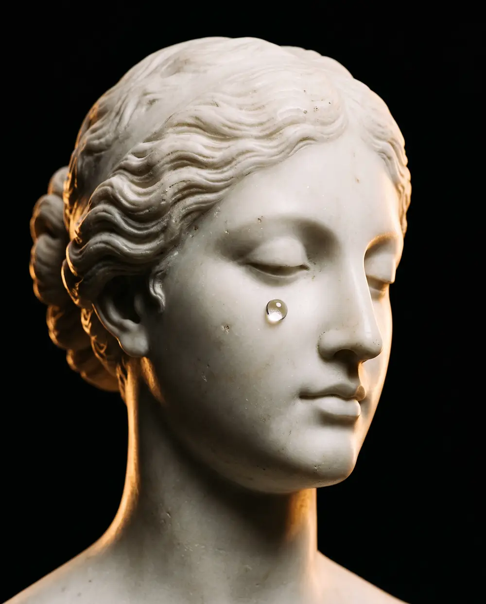 Rosto de estátua de mármore com uma gota de vidro, sob luz dourada